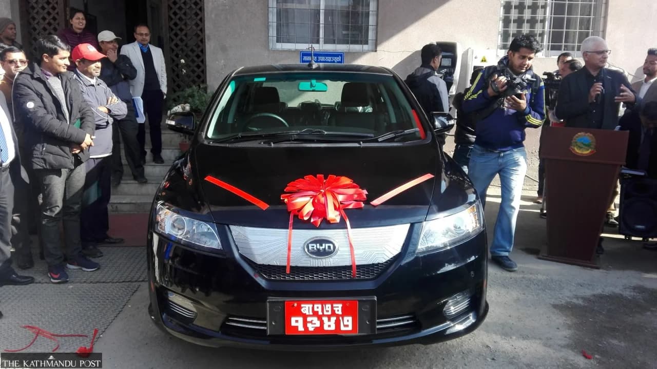 A black BYD electric car with a red ribbon on the hood, surrounded by people at an event.