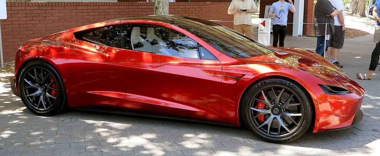 Tesla Roadster in red color, showcasing its sleek design and sporty wheels.